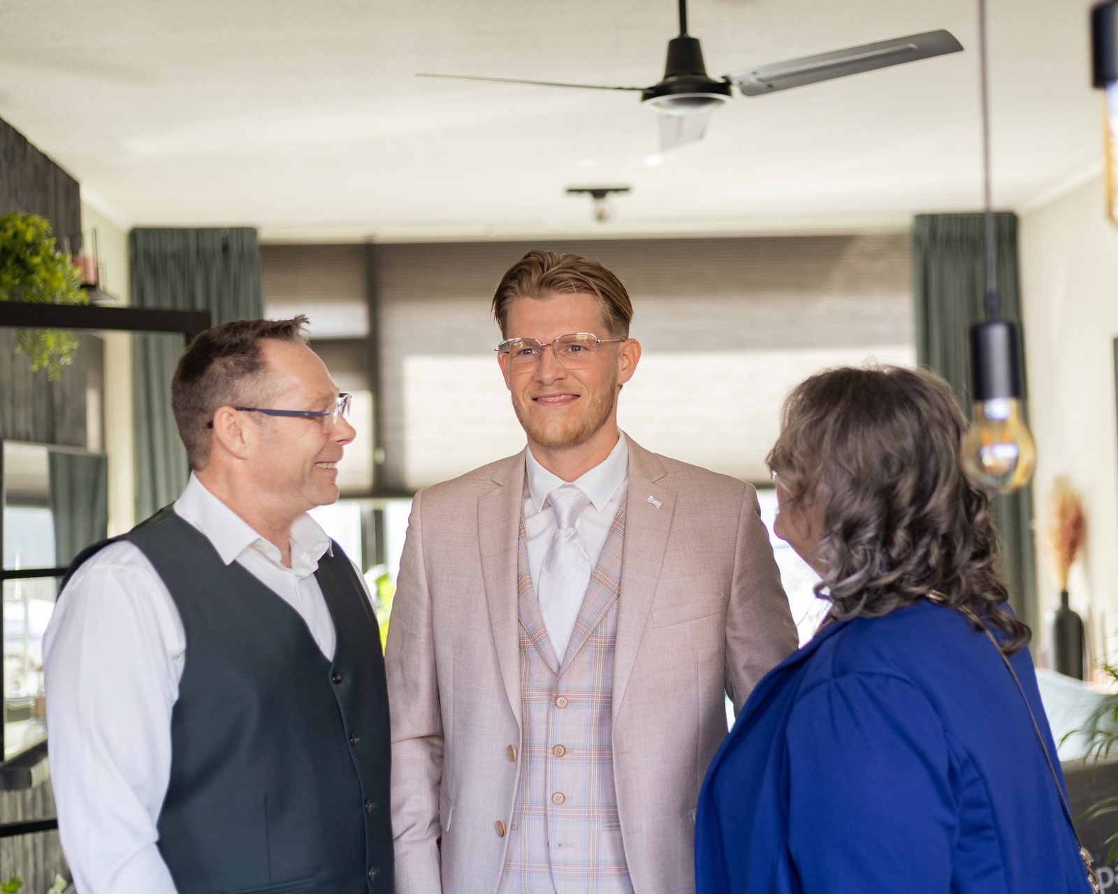 Bruidegom in licht pak deelt een ontspannen moment met zijn ouders op de trouwochtend — bruidsfotografie door Amped Productions